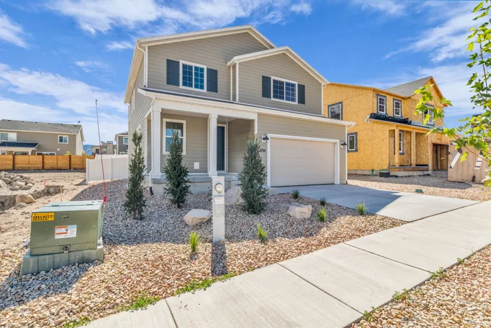 Two-story residence featuring light gray siding, dark shutters, an attached garage, a concrete driveway, and a front porch with pillars