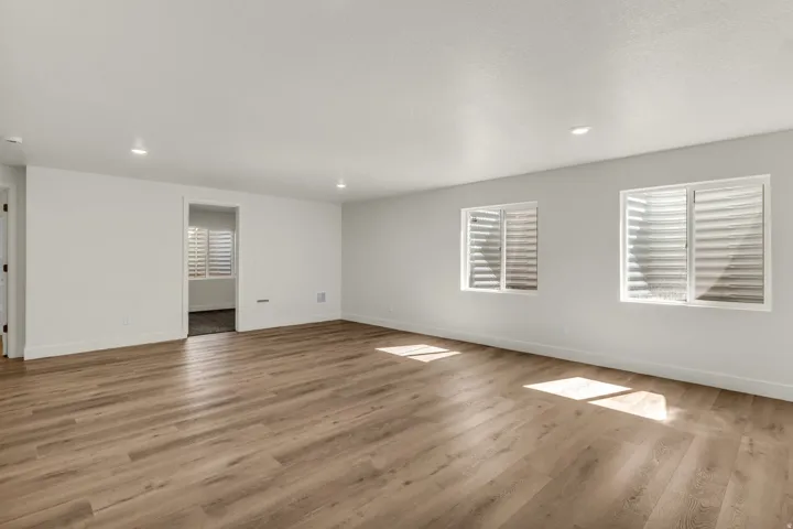 Spacious room with wood-finish flooring, recessed lighting, and two windows with horizontal blinds