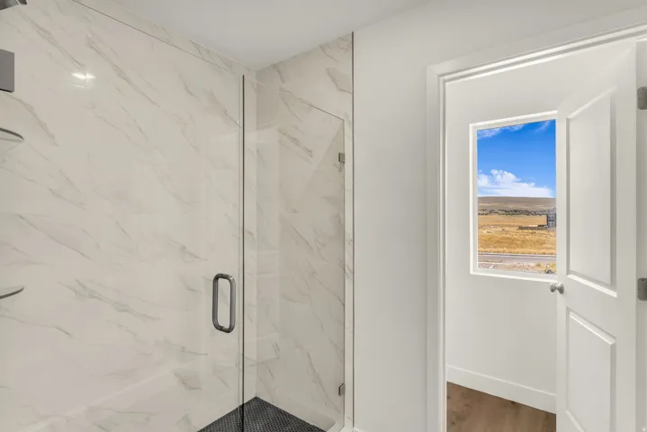 Glass-enclosed shower with full-height tile surround, black tile shower floor, and built-in corner shelving