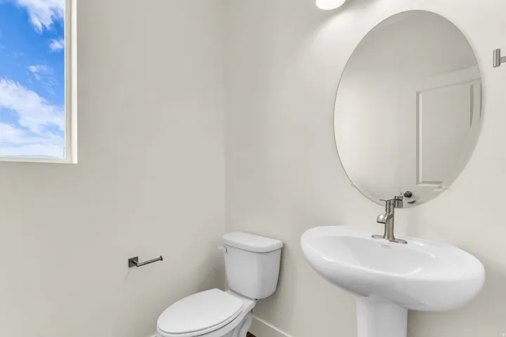 Pedestal sink with a brushed nickel faucet, wall-mounted oval mirror, and a window
