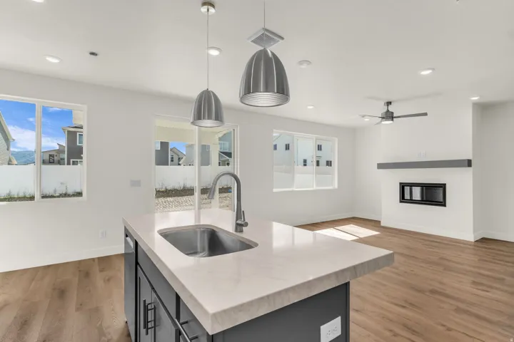 Central island with an undermount sink, pendant lighting, wood-finish flooring, recessed lighting, and a built-in fireplace