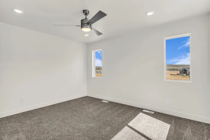Recessed lighting, ceiling fan with integrated light, two vertical windows, and grey carpeting