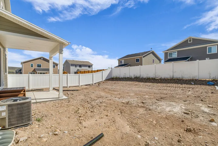 Covered patio with concrete flooring, framed by a white vinyl fence