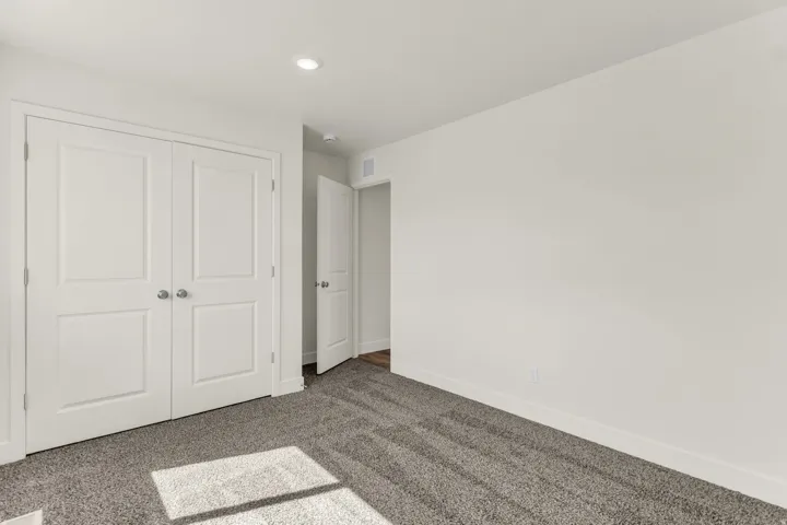 Recessed lighting illuminates neutral walls and gray carpet flooring
