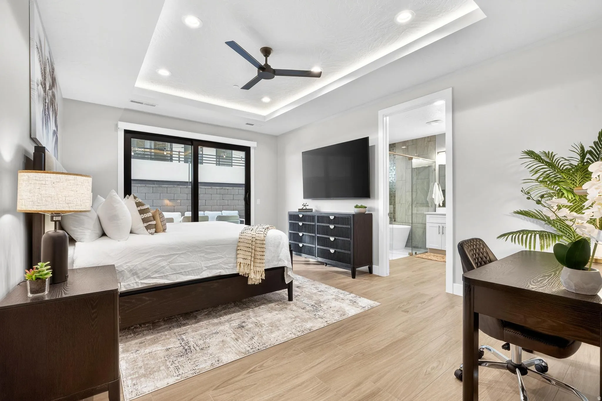 Recessed lighting, wood-finish flooring, tray ceiling with cove lighting, sliding glass door, and an integrated ceiling fan