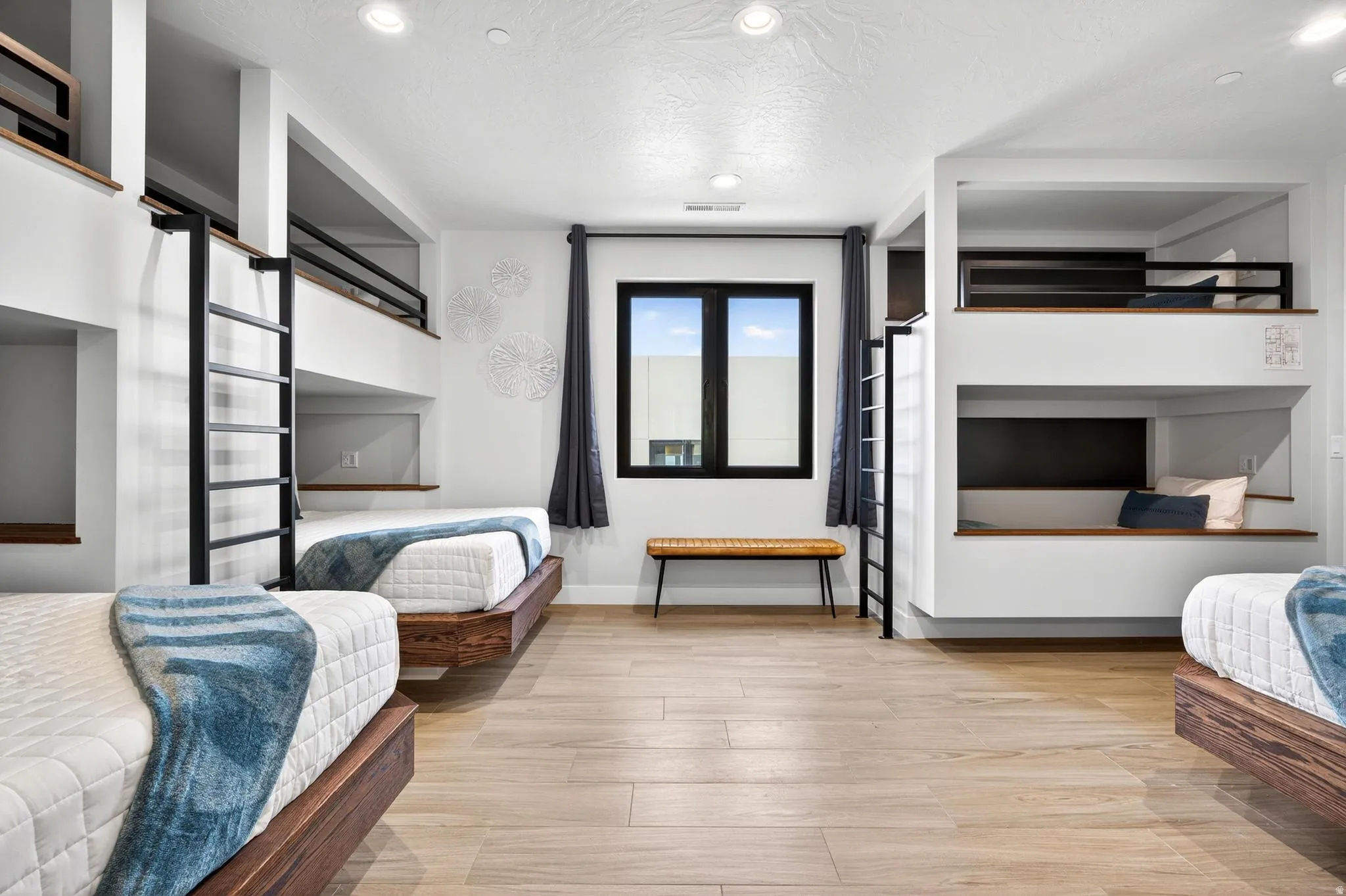 Built-in bunk beds with integrated ladders, recessed lighting, wood-finish flooring, and a large window with dark trim