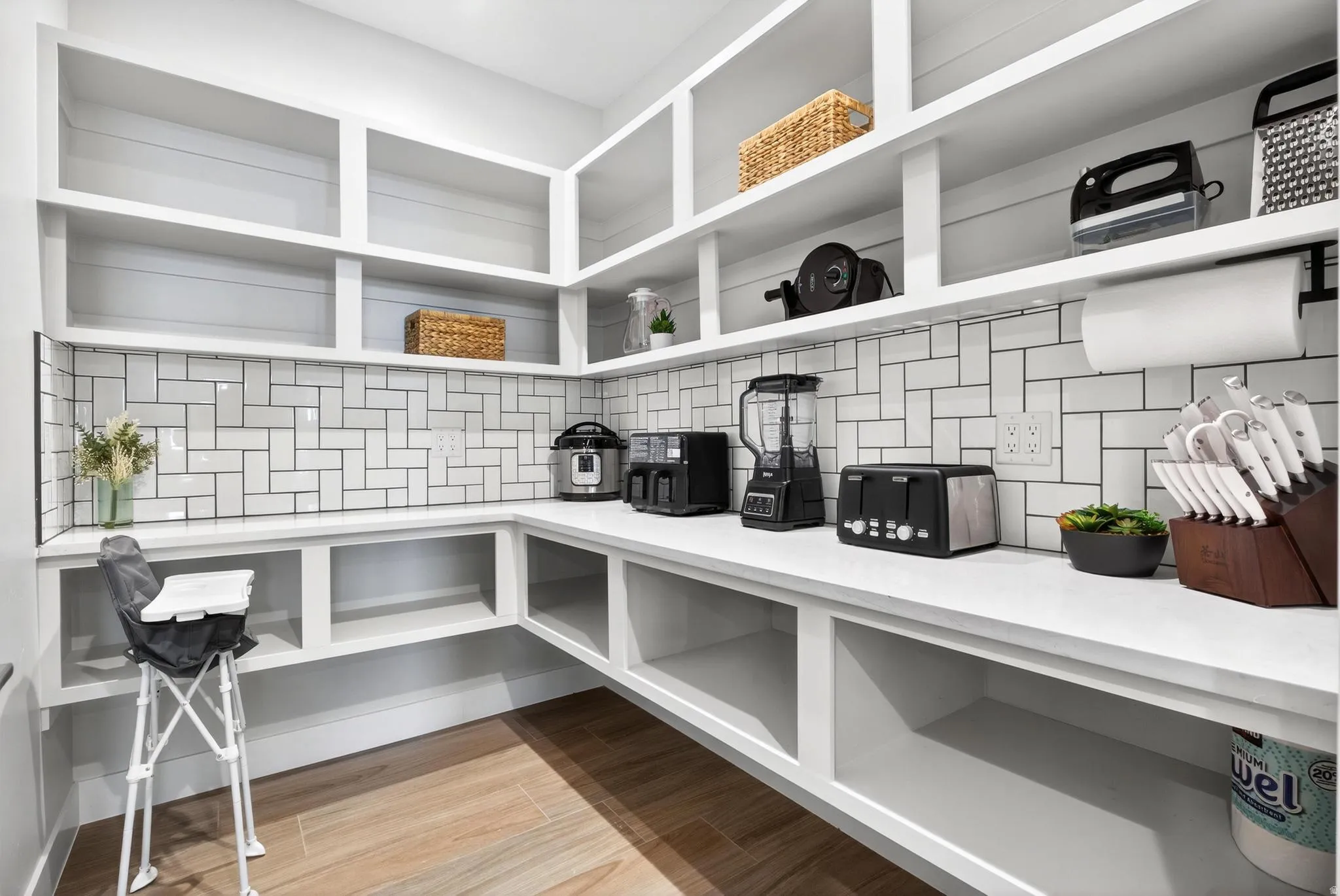 Built-in shelving, white subway tile backsplash, white countertops, wood-finish flooring, and multiple electrical outlets