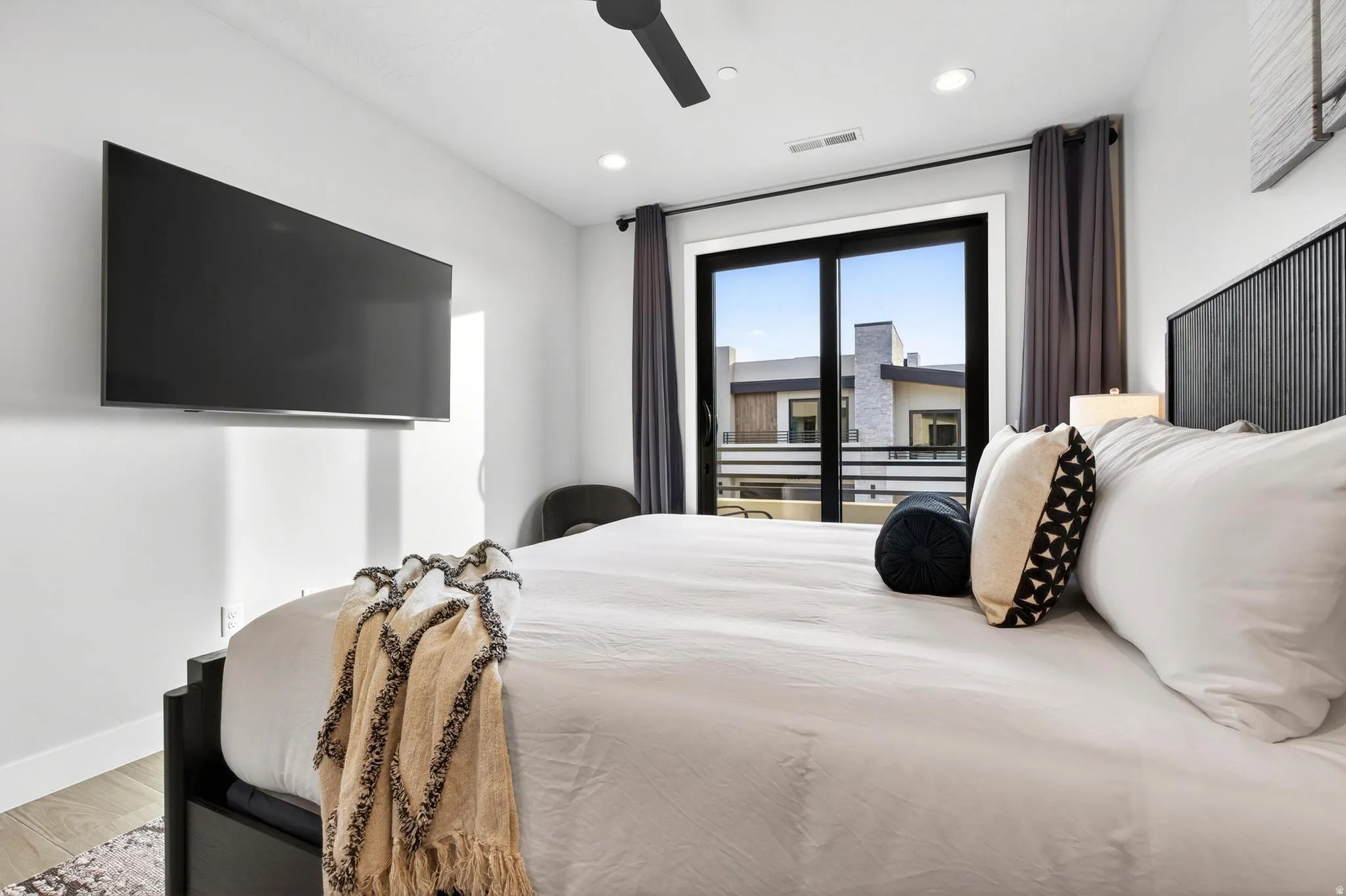 Recessed lighting, ceiling fan, wall-mounted television, full-light glass door, and dark drapery