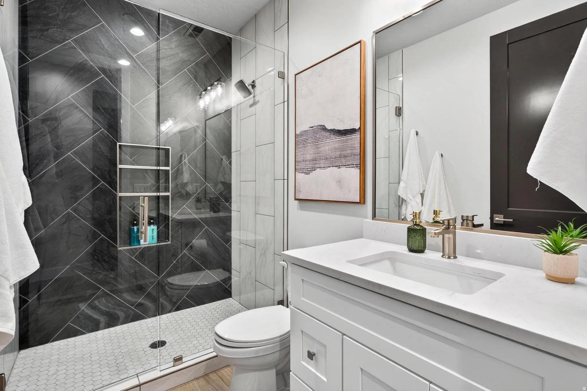 Walk-in shower with dark chevron-patterned tile, integrated shelving, and glass enclosure
