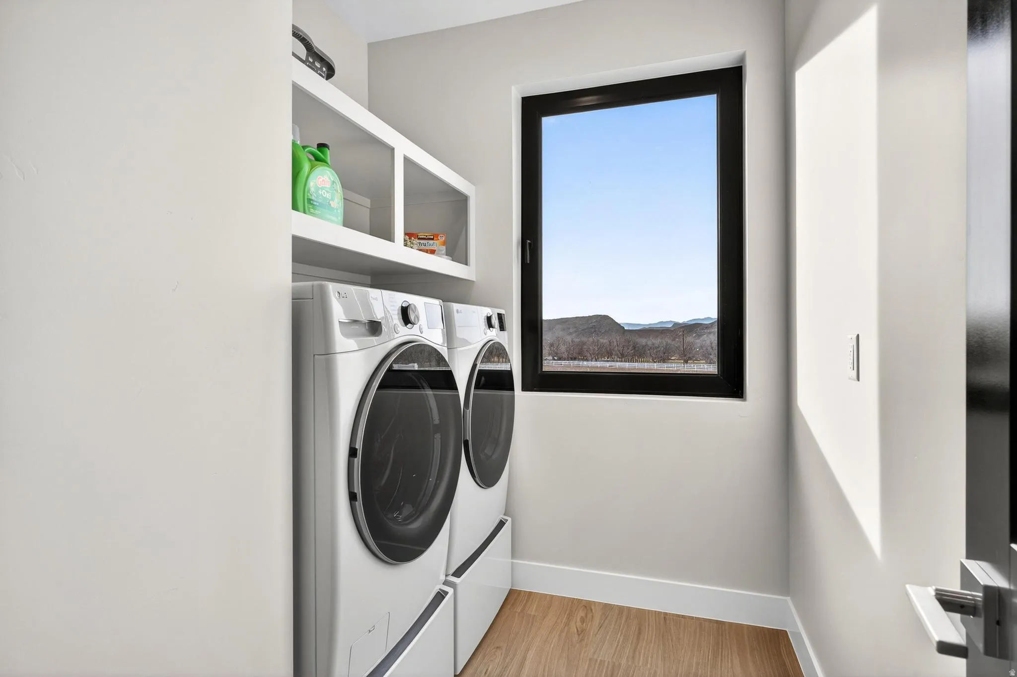 Dedicated laundry area with built-in shelving, two appliances, and wood-finish flooring