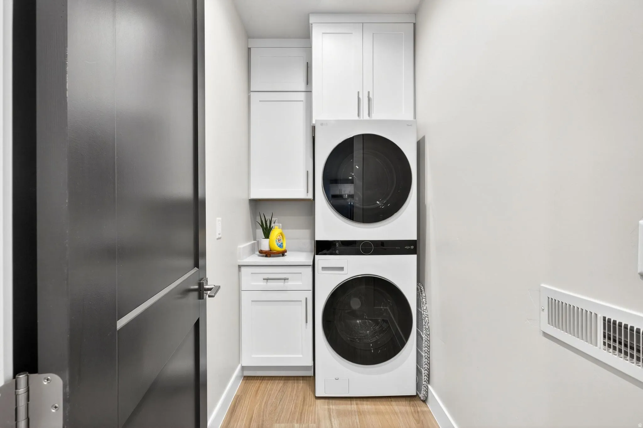 Stacked washer and dryer units, white cabinetry, wood-finish flooring, and a countertop
