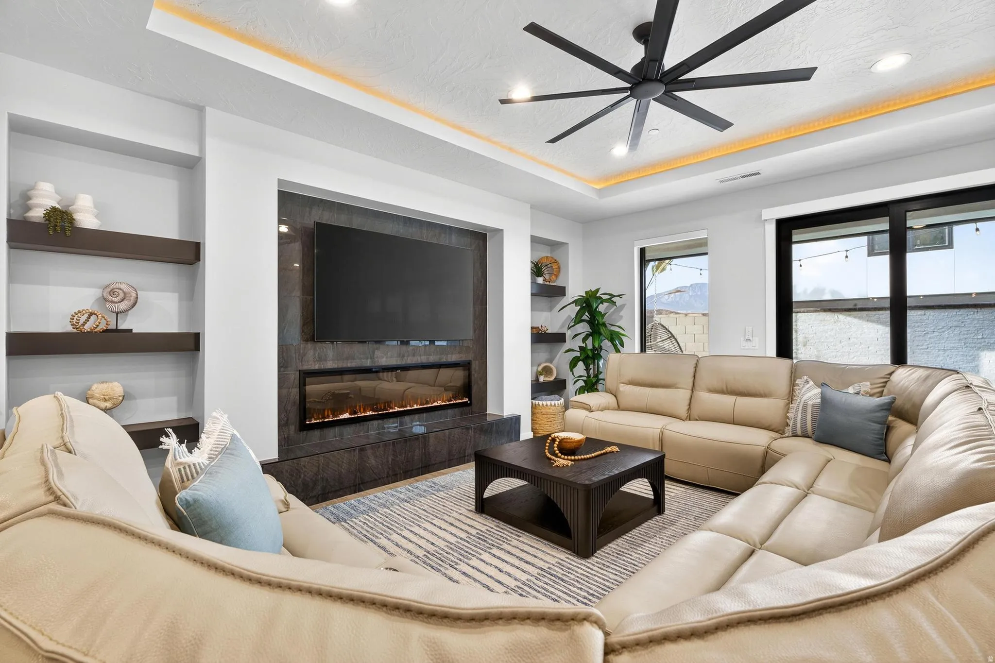 Recessed ceiling with integrated lighting, built-in shelving, an electric fireplace, and a contemporary ceiling fan