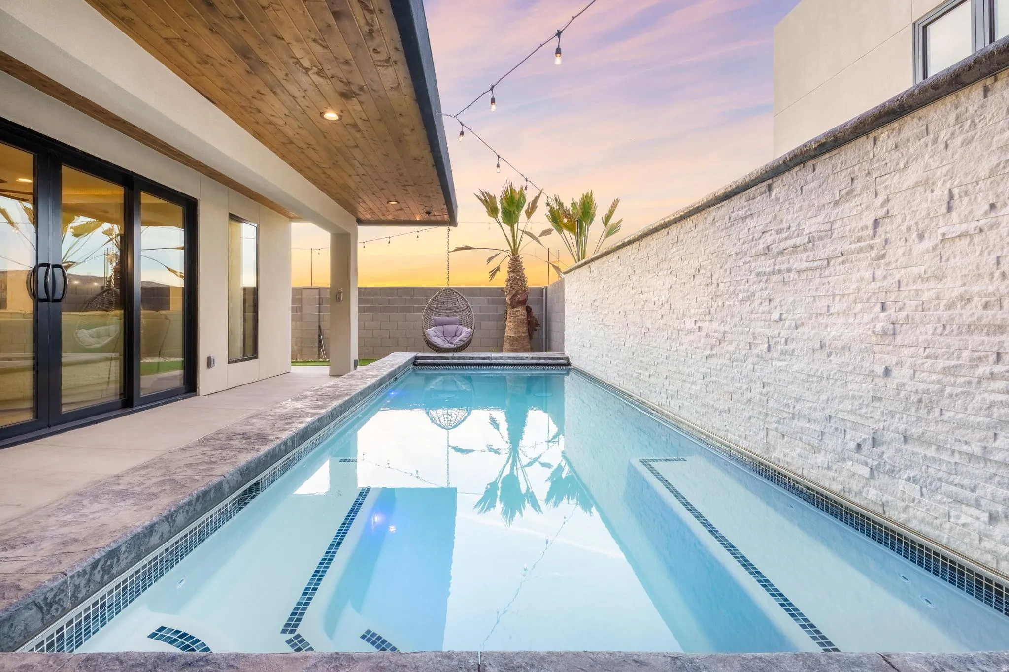 Plunge pool with mosaic tile accents, covered patio featuring a wood-finish ceiling, and floor-to-ceiling sliding glass doors