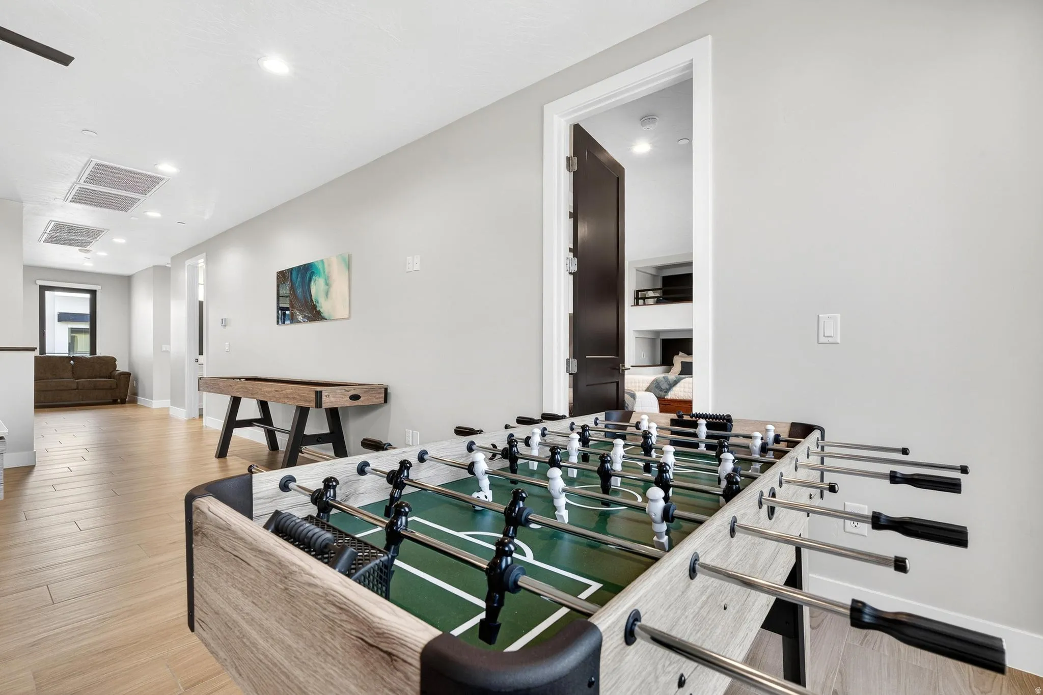 Dedicated recreation space featuring wood-finish flooring, recessed lighting, and a dark wood-paneled door