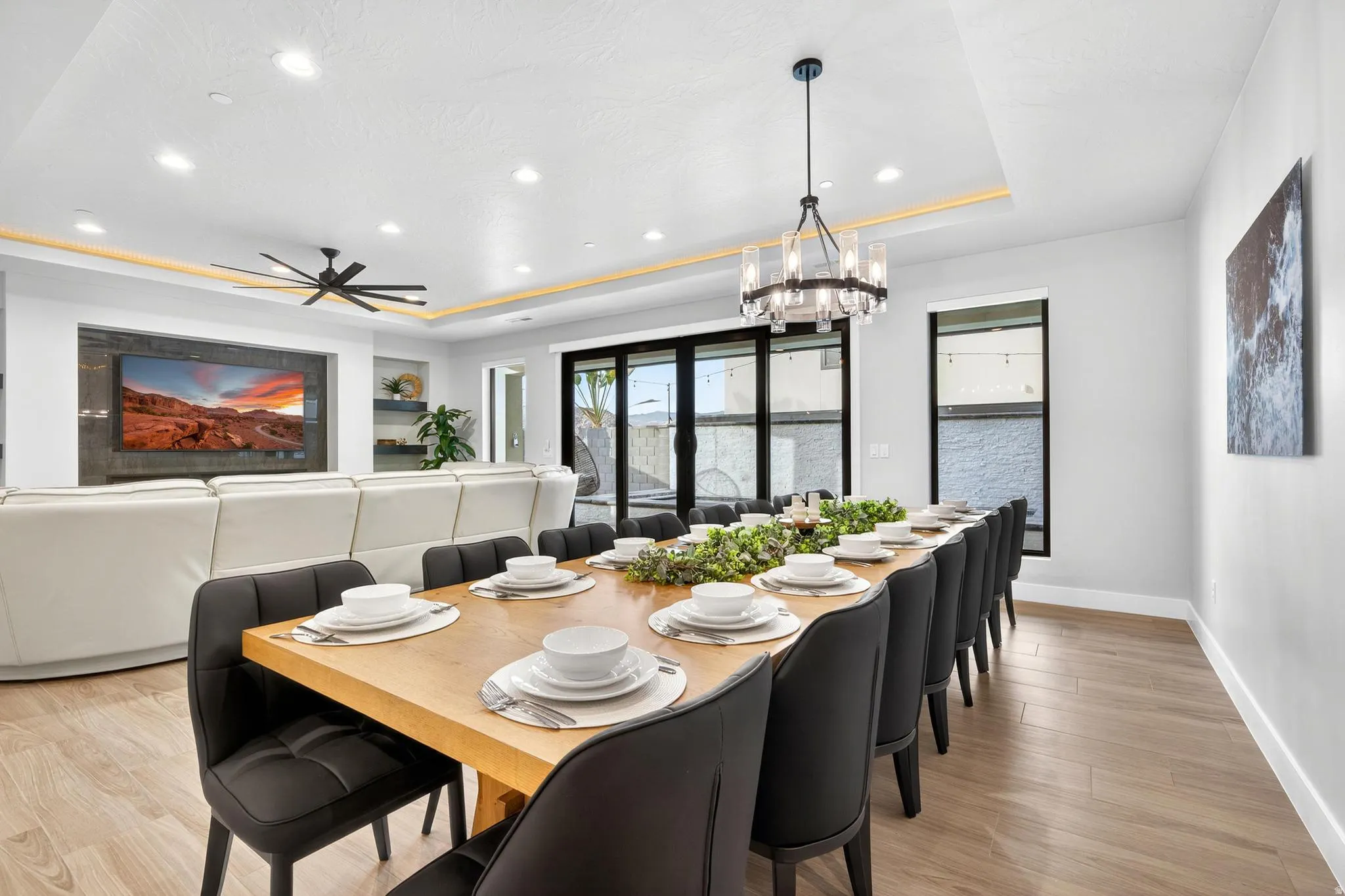 Tray ceiling with recessed lighting, wood-finish flooring, built-in shelving, sliding glass doors, and a linear chandelier