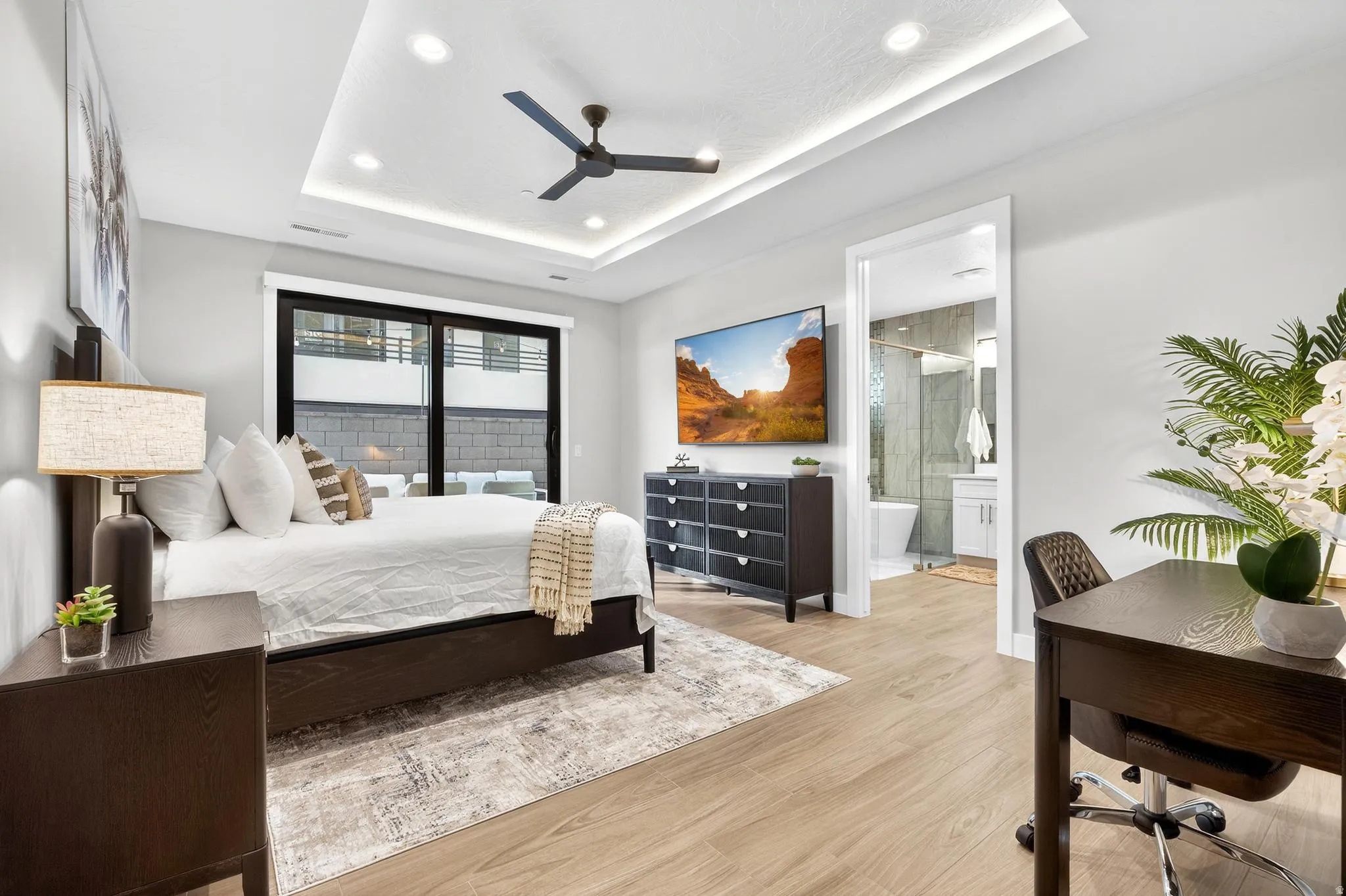Recessed ceiling with integrated lighting, wood-finish flooring, black frame sliding glass door, and an open doorway to a bathroom with a shower