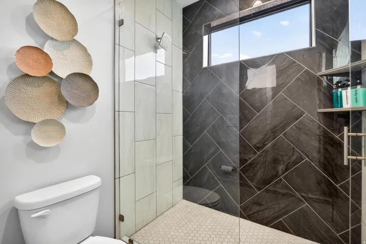Glass-enclosed shower with herringbone tile, hexagon-tiled floor, and a transom window