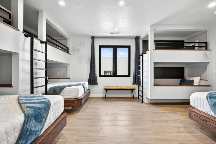 Built-in bunk beds with integrated ladders, recessed lighting, wood-finish flooring, and a large window with dark trim