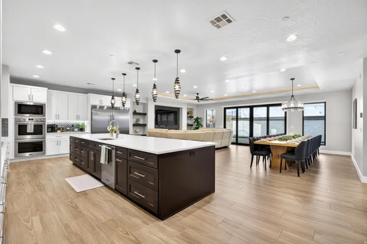 Expansive open-concept space featuring wood-finish flooring, a spacious kitchen island with a built-in dishwasher, stainless steel appliances, and large folding panel doors