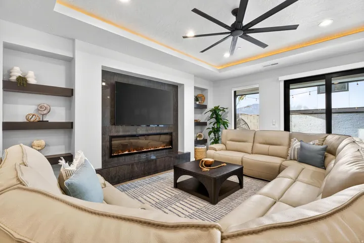 Recessed ceiling with integrated lighting, built-in shelving, an electric fireplace, and a contemporary ceiling fan