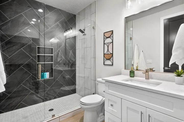 Glass-enclosed shower with dark stone-finish tile in a herringbone pattern and built-in shelving