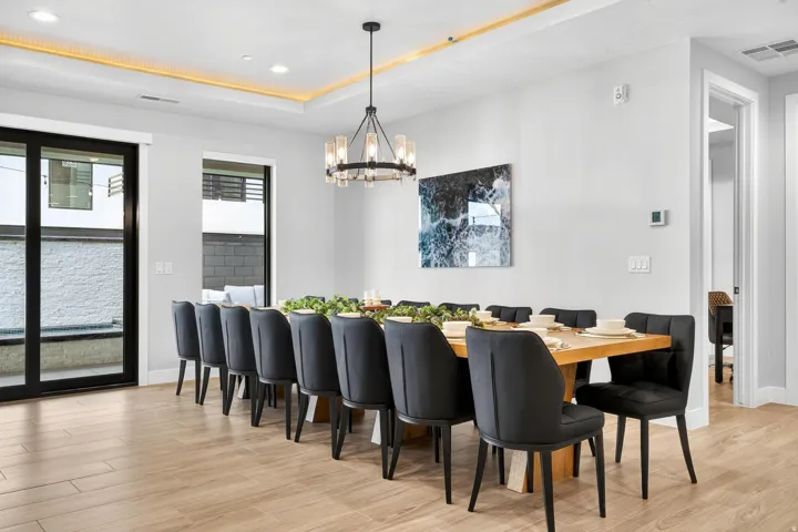 Tray ceiling with accent lighting, wood-finish flooring, glass sliding door, and contemporary chandelier