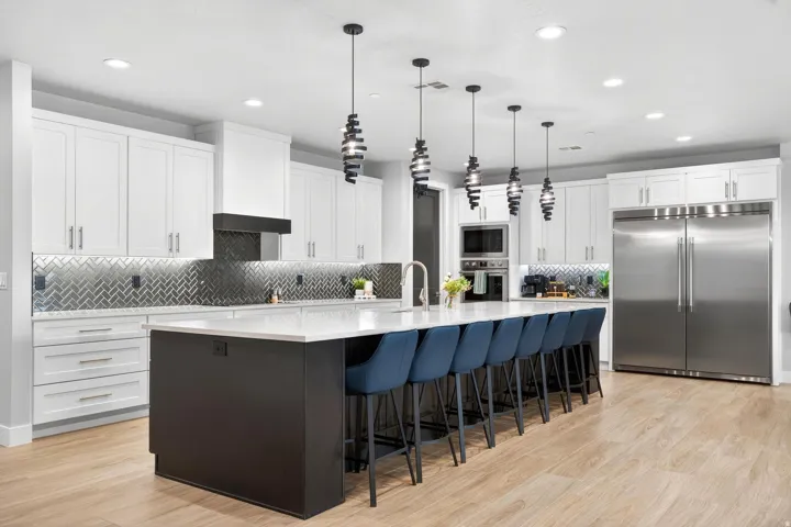 Kitchen featuring white cabinetry, a large kitchen island with a light-toned countertop, herringbone tile backsplash, wood-finish flooring, and stainless steel appliances