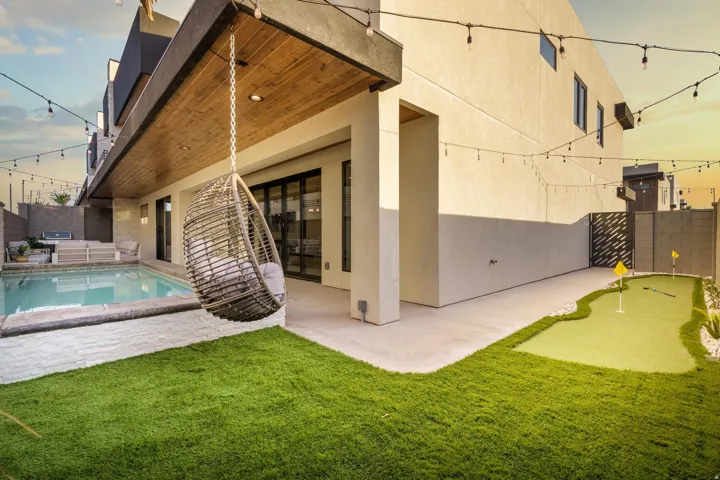 Expansive outdoor area featuring a swimming pool, a covered patio with wood-finish ceiling, a putting green, and artificial turf