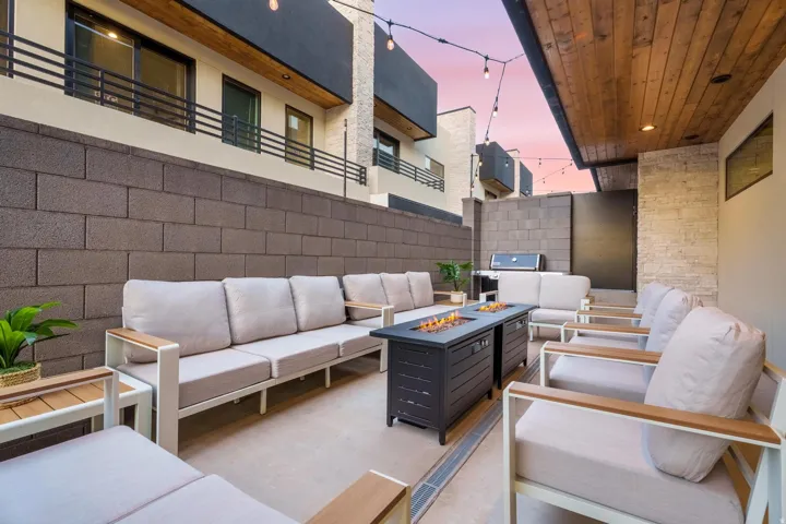Paved outdoor patio featuring a fire pit table, string lighting, and wood plank ceiling