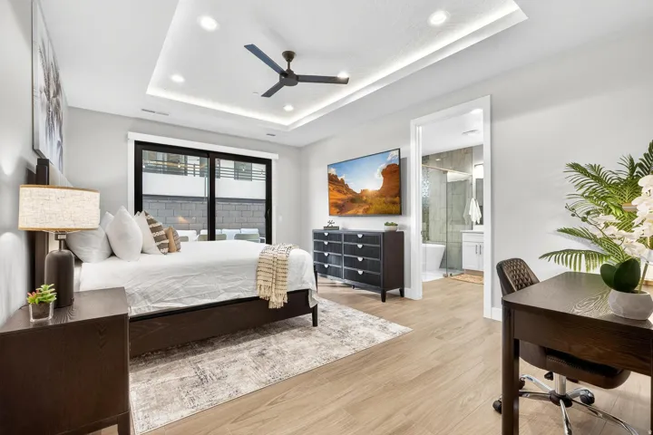 Recessed ceiling with integrated lighting, wood-finish flooring, black frame sliding glass door, and an open doorway to a bathroom with a shower