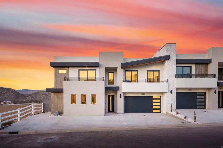 Modern architectural facade with a flat roofline, integrated two-car garage, multiple balconies with dark railings, and prominent vertical window features