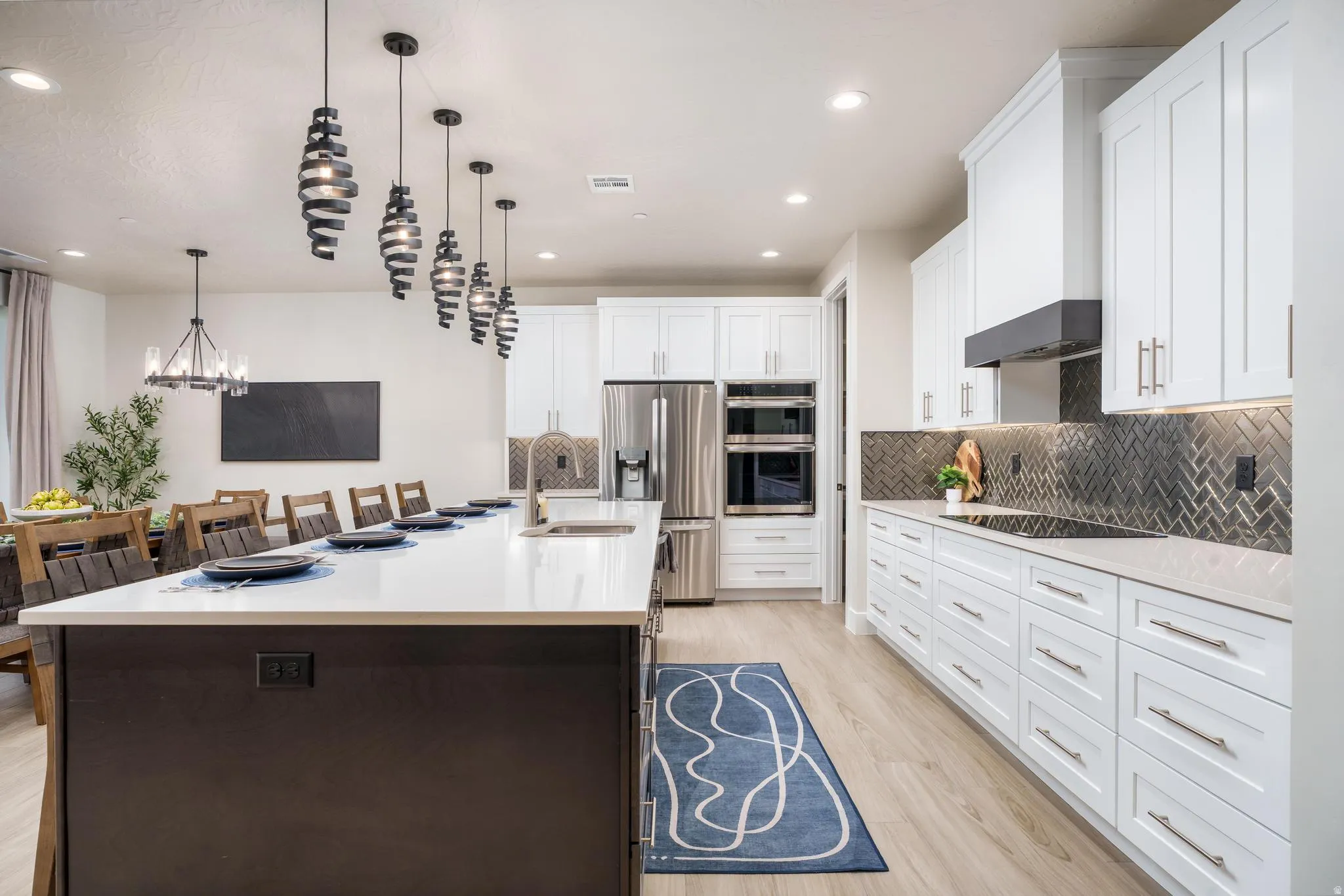 Spacious kitchen featuring a large island with sink, white shaker cabinetry, stainless steel appliances, and herringbone tile backsplash