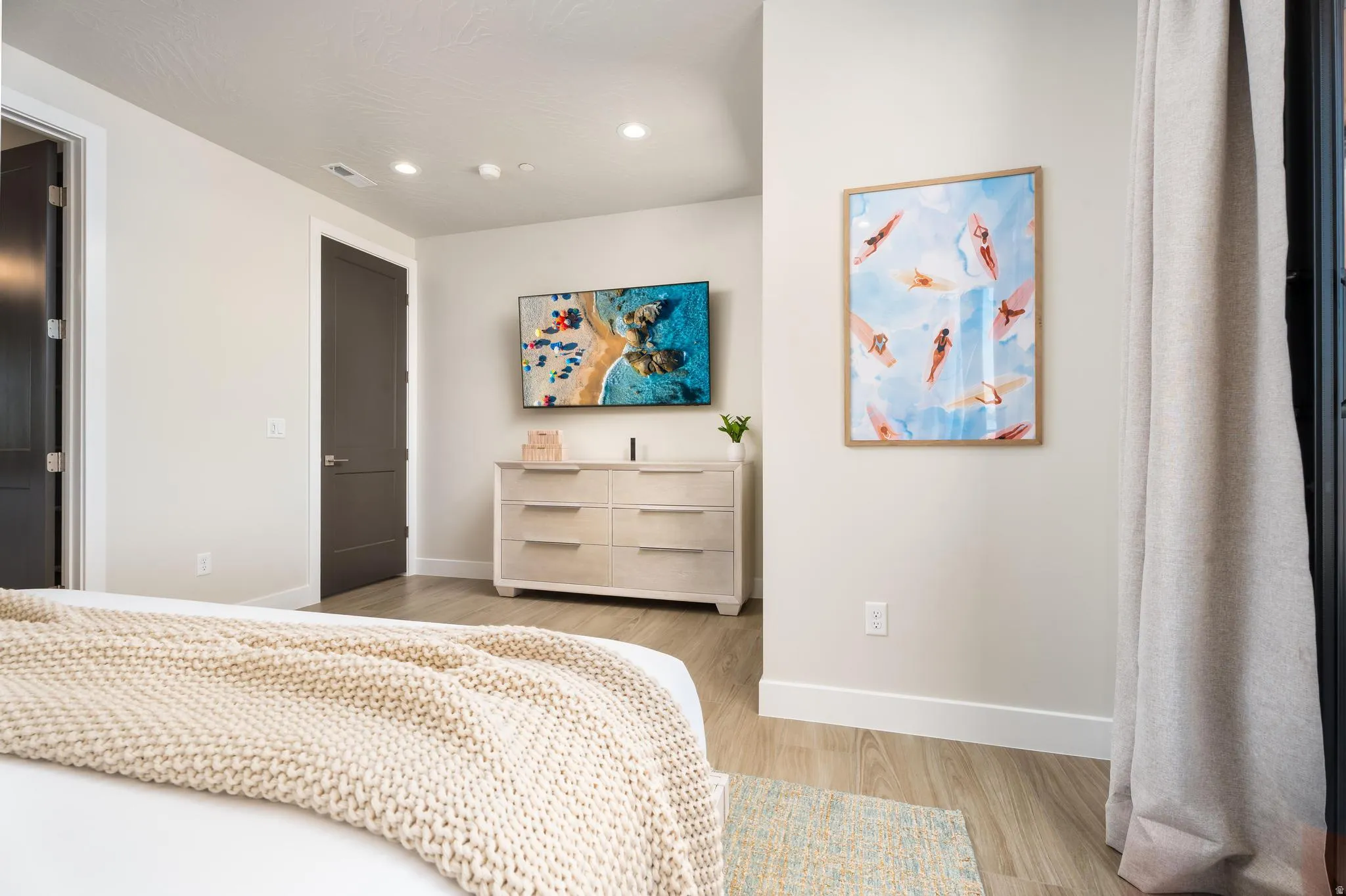 Recessed ceiling lighting, wood-finish flooring, a wall-mounted television, and a dark-paneled door
