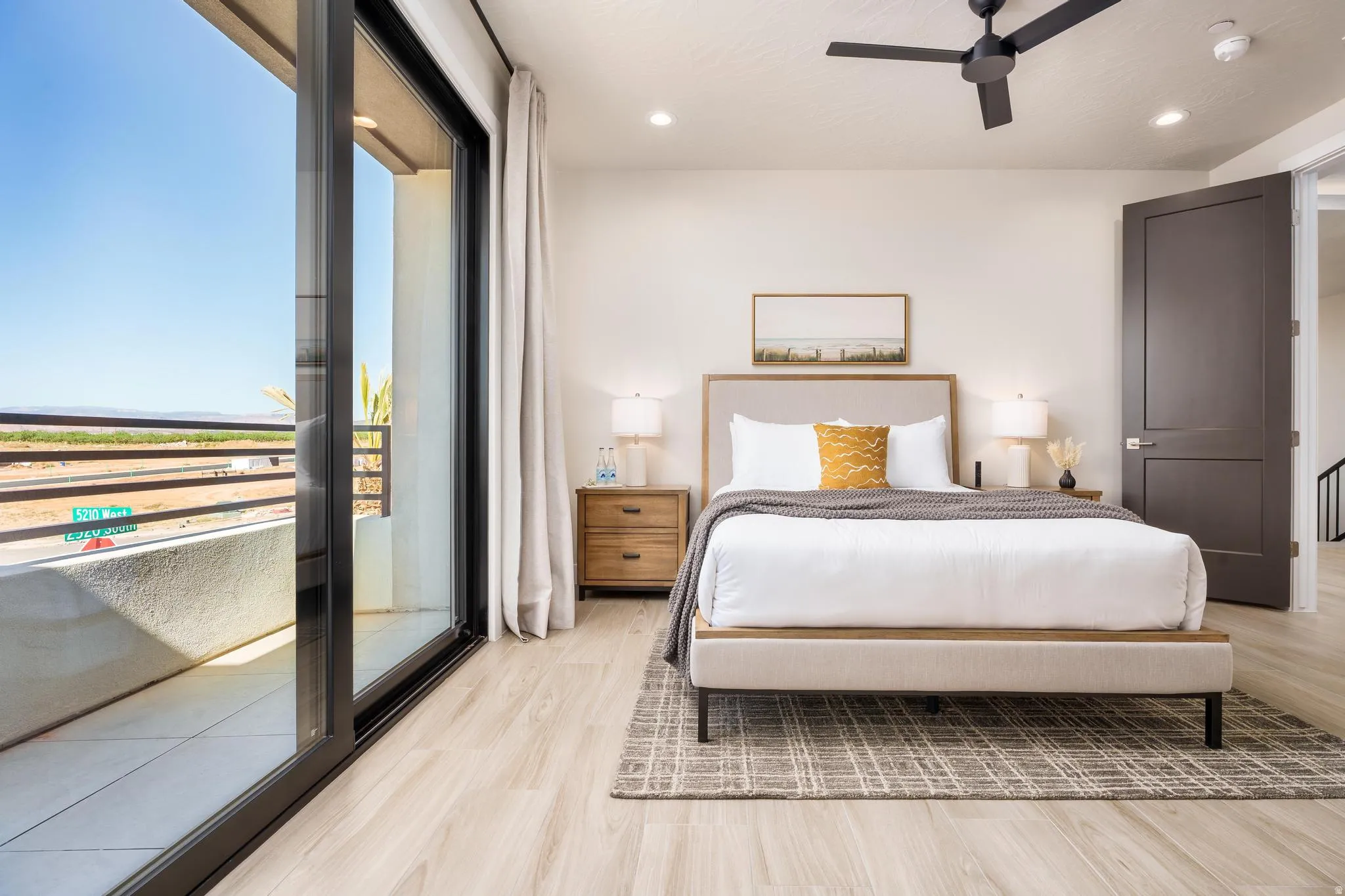 Spacious room featuring wood-finish flooring, a contemporary ceiling fan, recessed lighting, and a large sliding glass door opening to a private balcony with metal railings