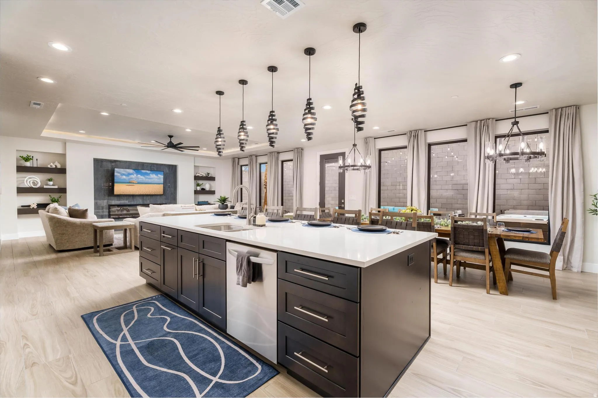 Spacious open-concept living area featuring an expansive kitchen island with a white countertop, dark wood-finish cabinetry, and pendant lighting