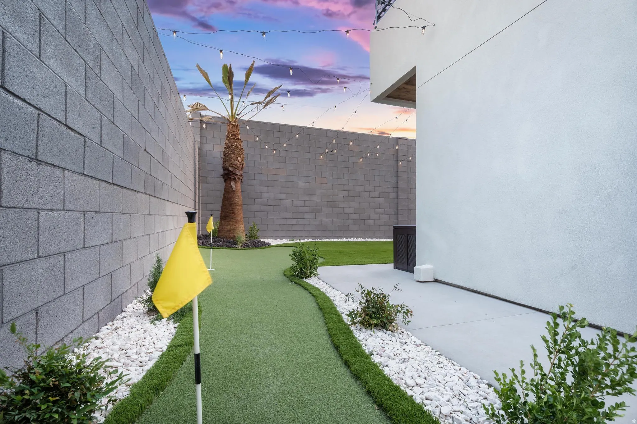 Putting green, paver patio, block walls, string lights, and established palm