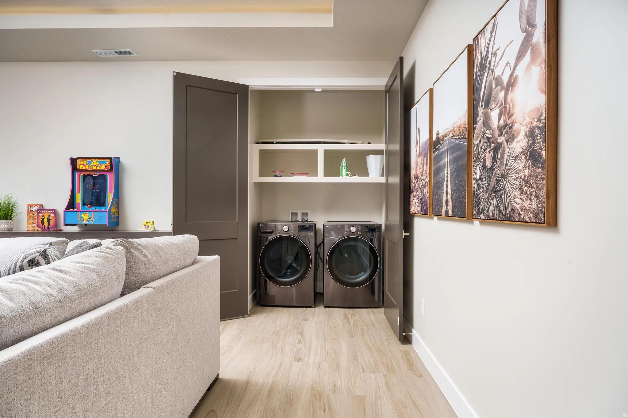 Built-in laundry closet with stacked shelving, modern dark-finish washer and dryer, and light wood-finish flooring