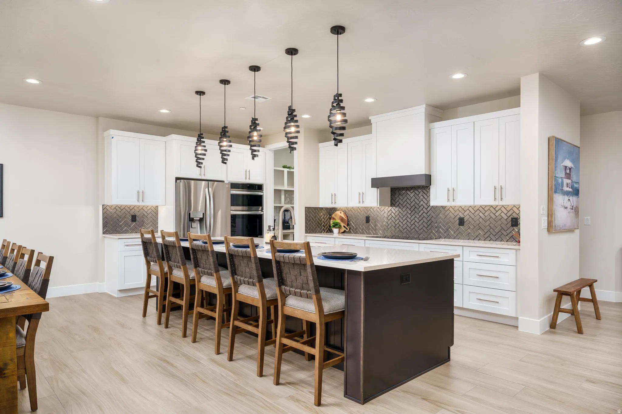 Kitchen featuring white cabinetry, stainless steel appliances, a dark herringbone backsplash, a central island with seating, and pendant lighting
