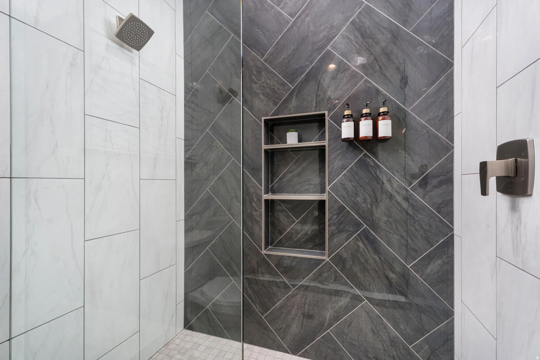 Spa-inspired shower enclosure featuring large-format charcoal tile with diagonal layout, frameless glass partition, dual built-in niches with shelving, and contemporary wall-mounted fixtures