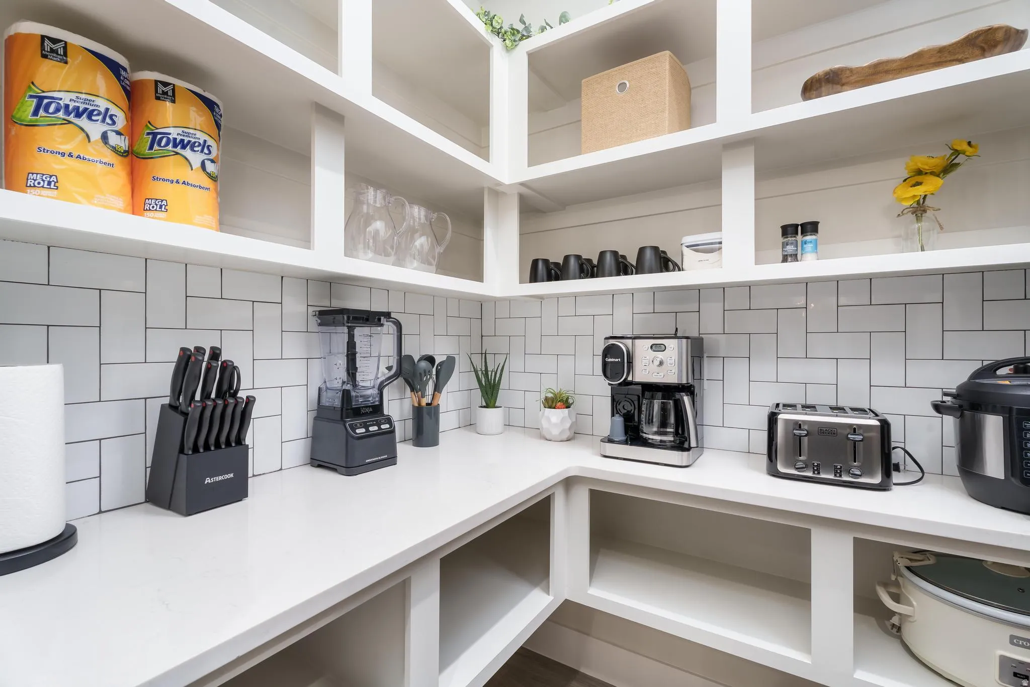 White subway tile backsplash, white countertops, built-in shelving, and open storage