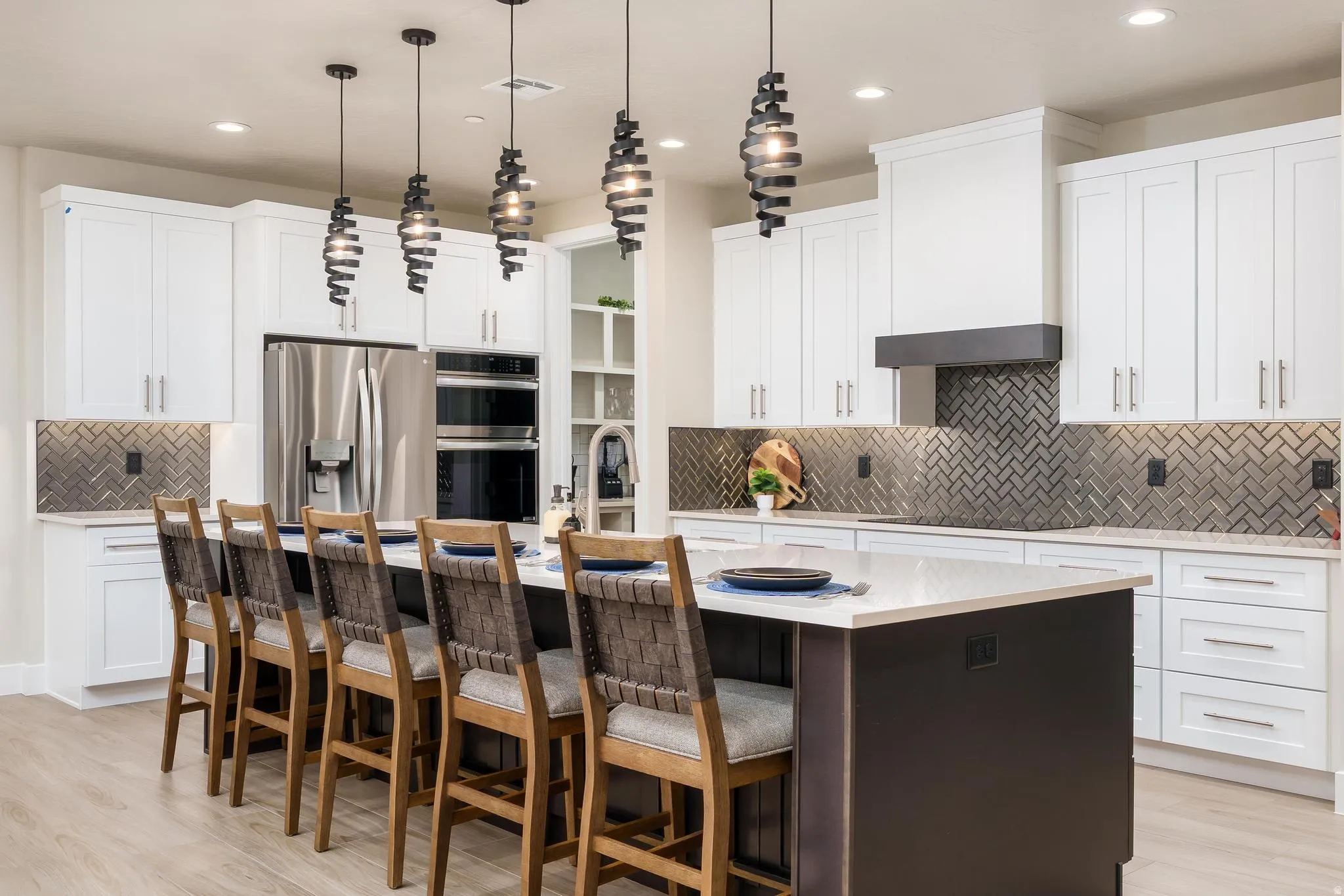 Gourmet kitchen with stainless steel appliances, herringbone tile backsplash, white shaker cabinetry, and a large island featuring pendant lighting