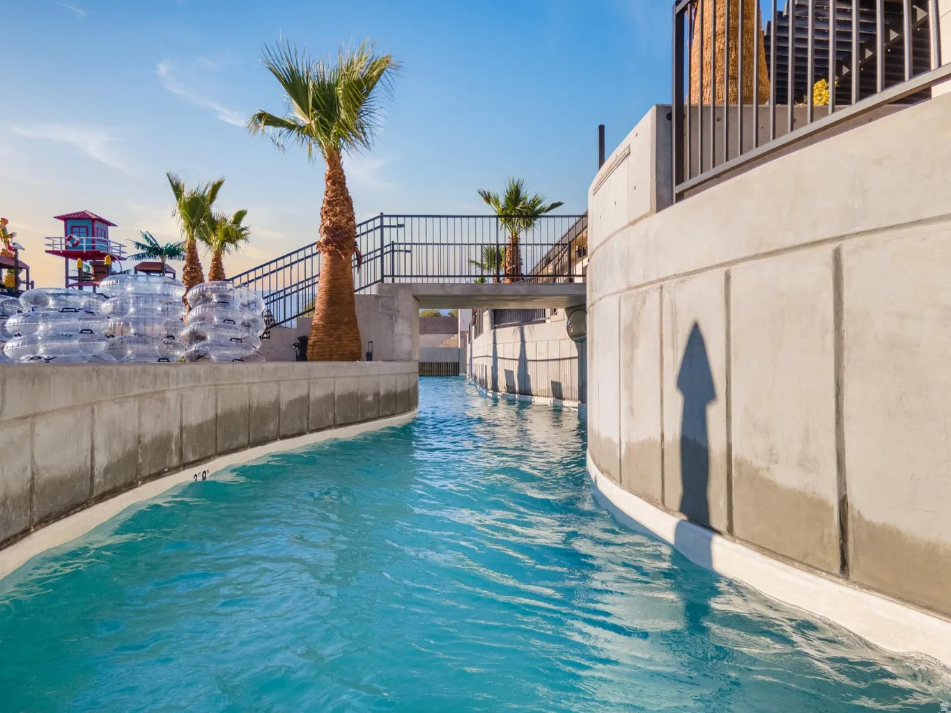 Curved concrete walls framing a water feature, multiple palm trees, and a black metal railing