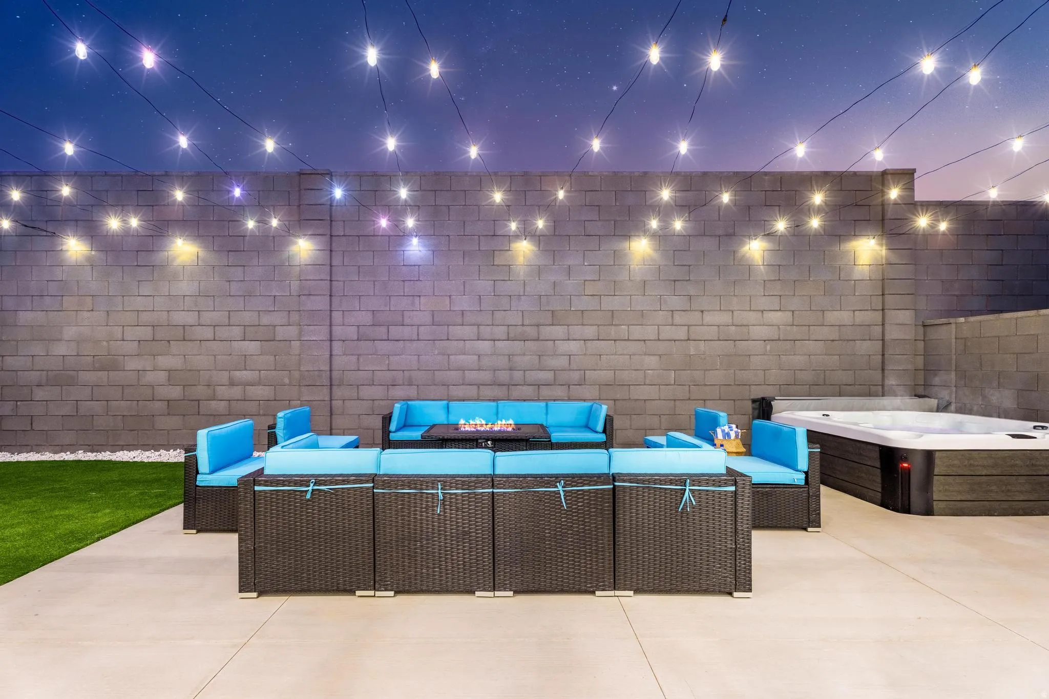 Expansive paved patio with a built-in spa, artificial turf section, string lighting, and concrete block privacy walls