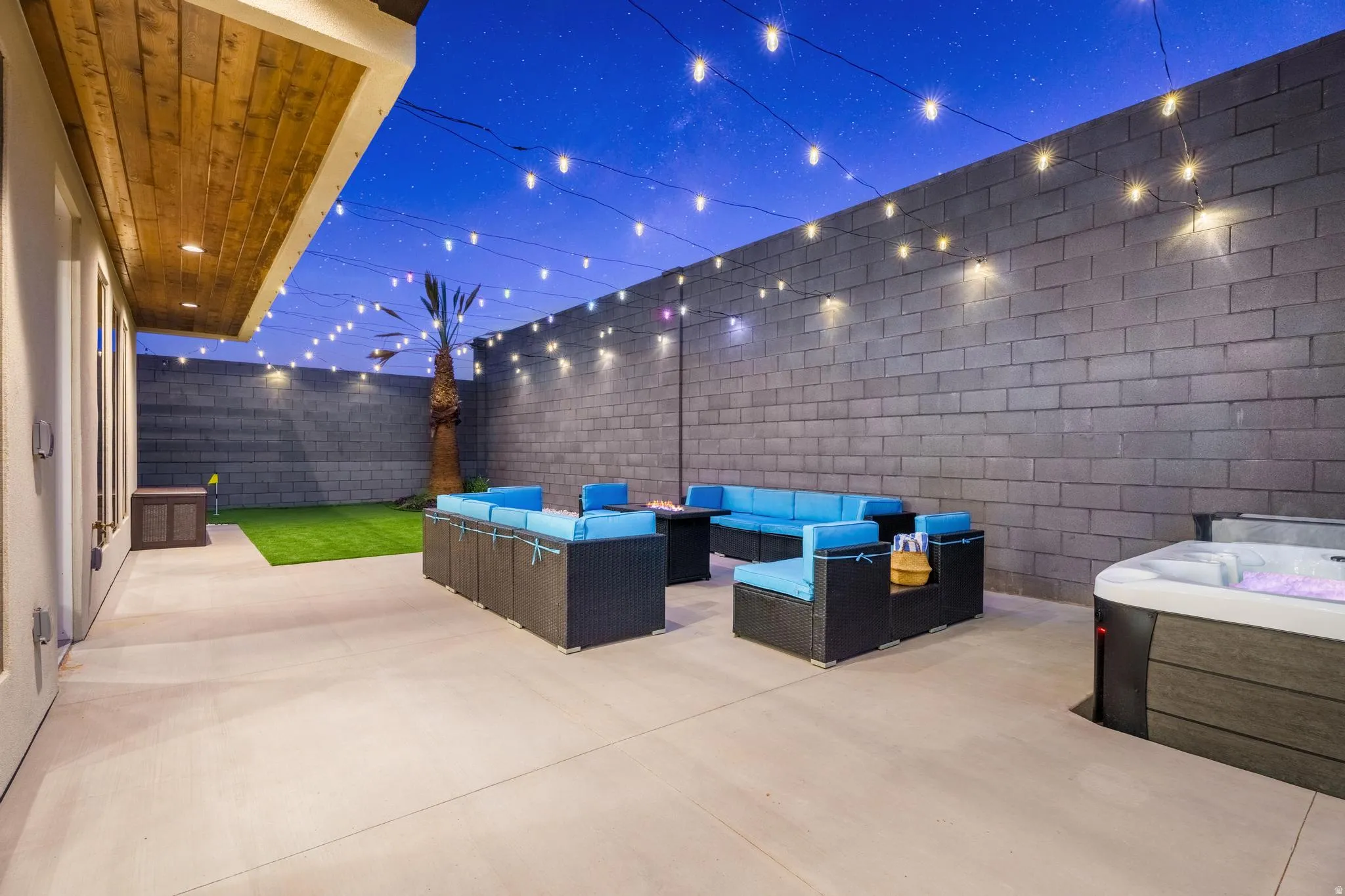 Private outdoor living area featuring a hot tub, string lighting, and an artificial turf lawn