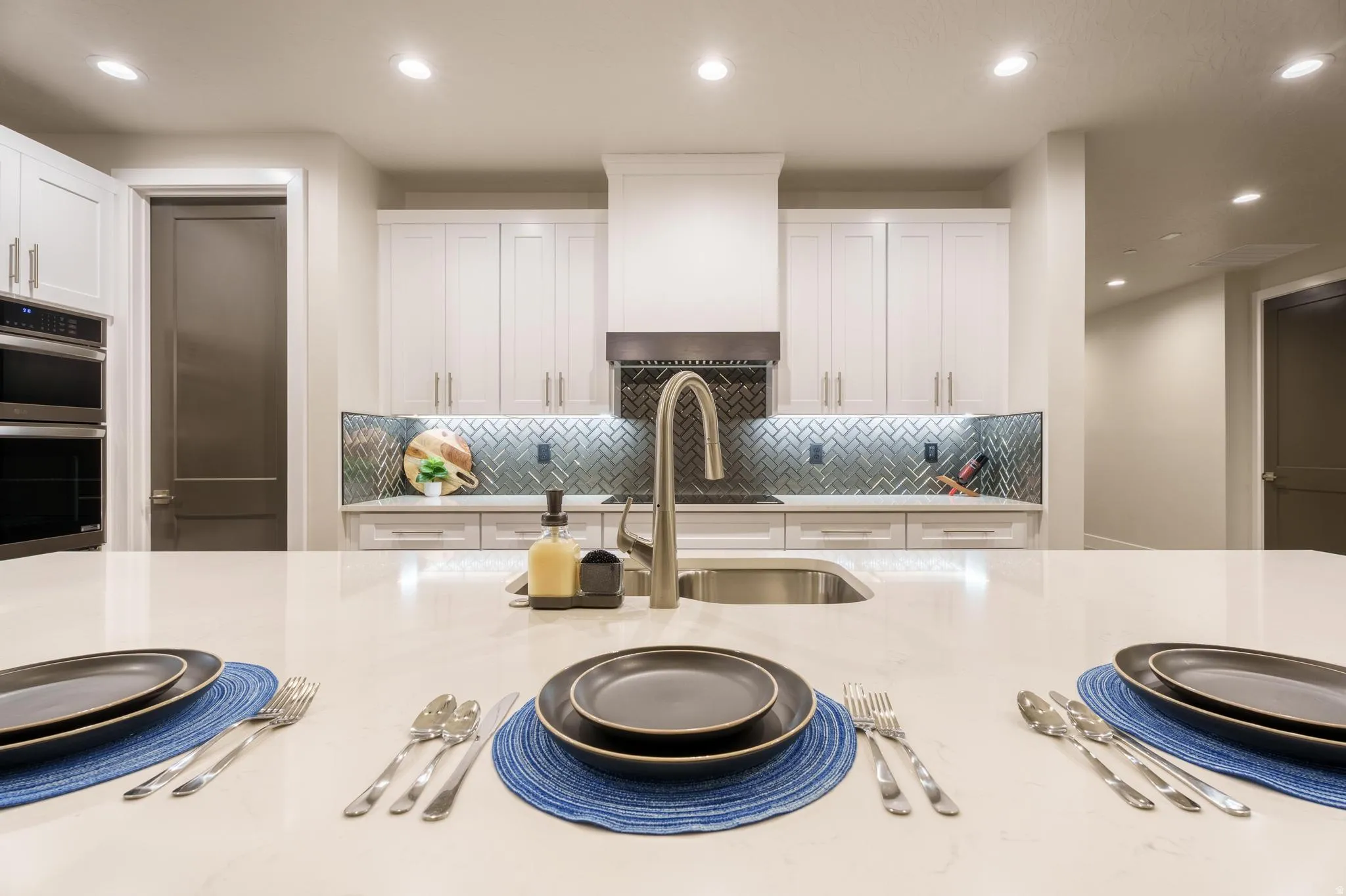 Kitchen featuring a large island with a built-in sink, stainless steel appliances, white cabinetry, and a herringbone pattern tile backsplash