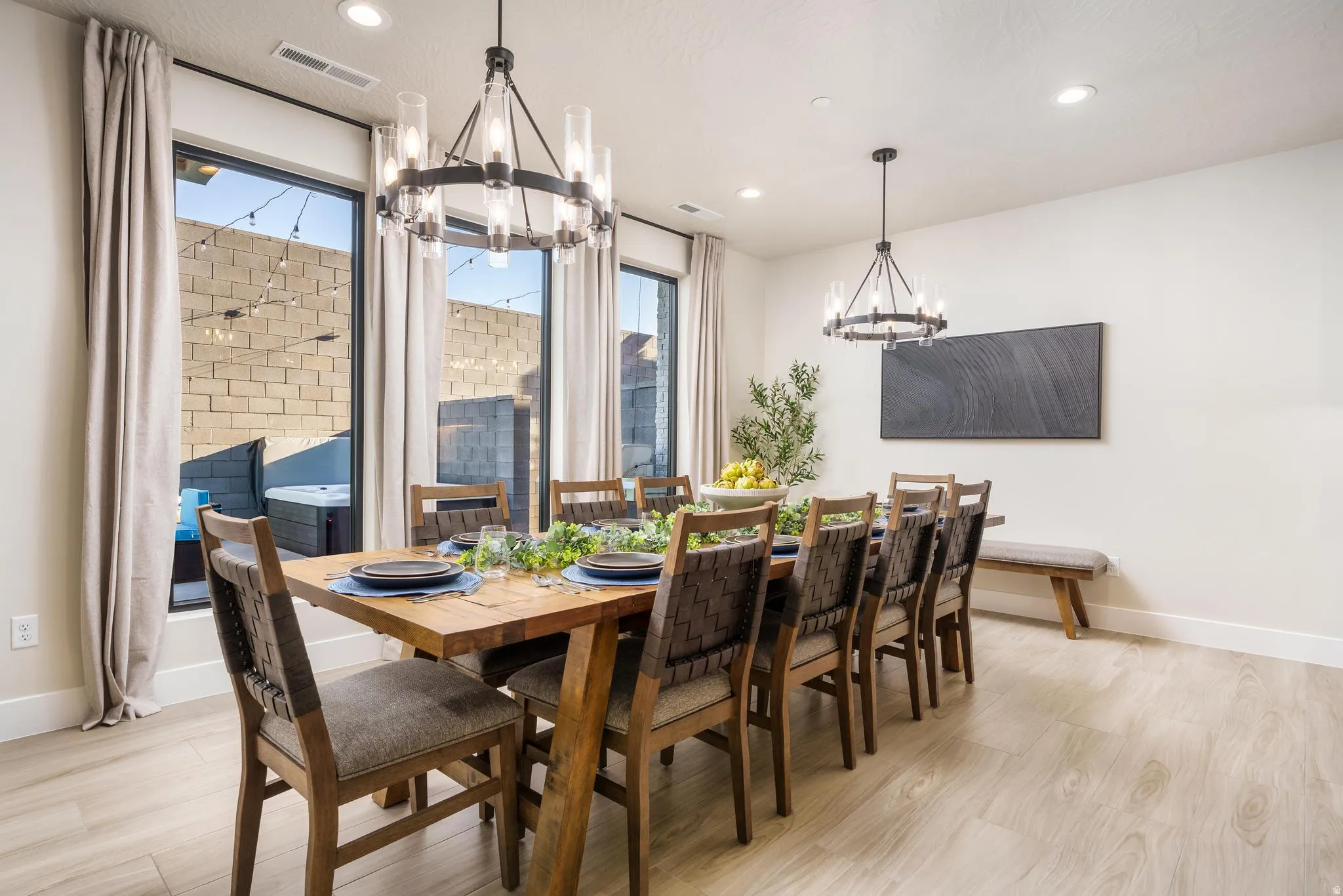 Wall-to-wall windows, two contemporary chandelier light fixtures, recessed ceiling lights, and wood-finish flooring