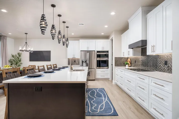 Spacious kitchen featuring a large island with sink, white shaker cabinetry, stainless steel appliances, and herringbone tile backsplash