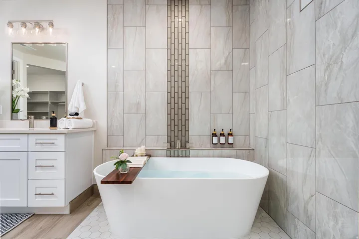 Freestanding soaking tub, white shaker vanity with drawer storage, polished chrome hardware, quartz countertop, and large format wall tiling