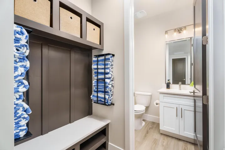 Built-in bench with storage, overhead shelving, board and batten paneling, vanity with white shaker-style cabinetry, and a modern light fixture