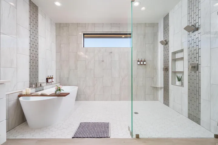 Freestanding soaking tub, walk-in shower with glass enclosure, dual shower heads, recessed shelving, and a horizontal window